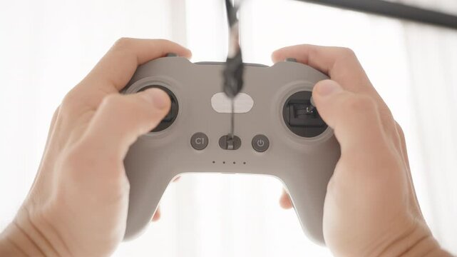 Person Holding and Tilting FPV Drone Controller with Cable in Bright Backlight, Front Low Angle, Drone Operation Concept