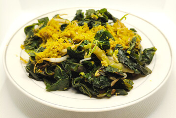 A plate of traditional vegetable dish with leafy greens, bean sprouts, grated coconut, and spices. A flavorful and healthy meal rich in nutrients, served on a simple white plate.