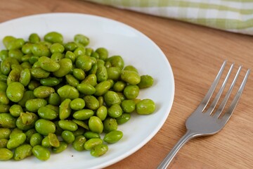 A plate of green Edamame soy beans on a table with a fork near it