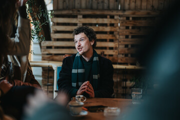 A man sits at a wooden table in a rustic cafe, engaged in conversation. Natural lighting and warm colors enhance the scene, creating an inviting atmosphere perfect for social interactions.