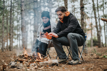 A cozy picnic takes place in the woods, with a group warming hands by the fire and enjoying nature...