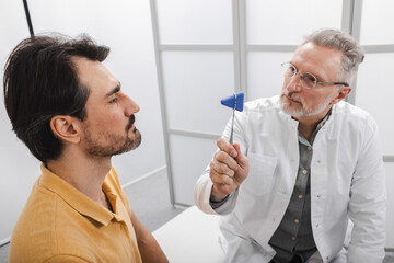Obraz premium Neurologic examination. Doctor neuropathist check-up male patient's nervous system and reflexes using neurological hammer in medical office