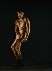 Naklejka premium A person standing in an artistic pose under focused studio lighting, highlighting their well-defined physique. The minimalist setting emphasizes artistic expression and body aesthetics.