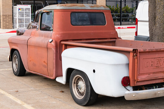 An old school truck with a patchwork paint job. The paint is mainly reddish orange.