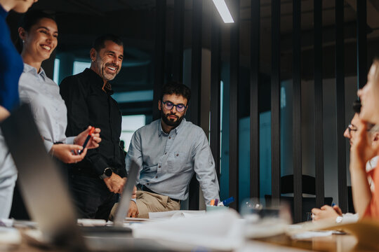 A diverse group of business colleagues brainstorming ideas and solutions during a late evening meeting. The team discusses projects and strategies, creating a productive and inclusive work environment