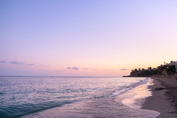 Landscape at sunset of a town in southern Spain. The beach empty and the Mediterranean Sea is calm. The waves wet the shore and palm trees are cut against the pink and violet sunset sky © LaMorenita