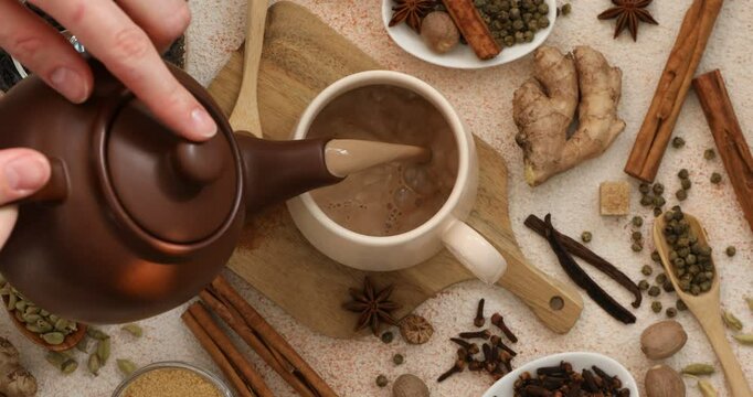 Woman pouring aromatic Masala tea into cup at color textured table, top view