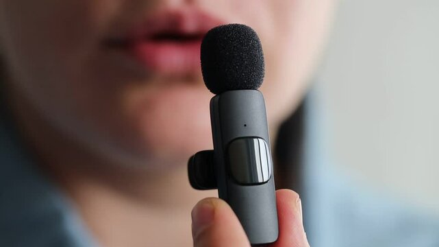 Woman talking into lavalier microphone on light grey background, closeup