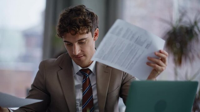 Smiling creator looking papers sitting laptop table workplace in office closeup