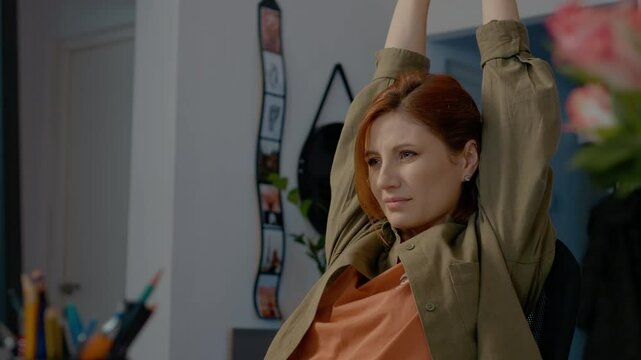While working at her home office, a woman experiences discomfort and stretches to alleviate back pain and numbness caused by long hours of sitting.