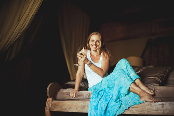Obraz premium Young woman sit on sofa inside luxury wooden villa. Girl relaxing on family summer vacation. Tropical lifestyle.