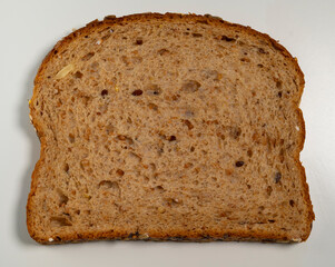 Slice of brown whole grain bread with seeds on white background