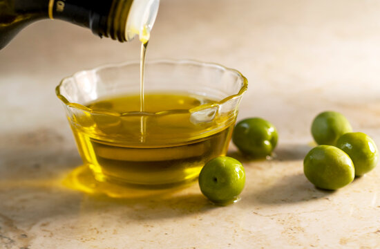 Olive oil pouring into small glass bowl with olives on table