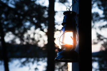 Kerosene lantern hanging by lakeside camp at sunset