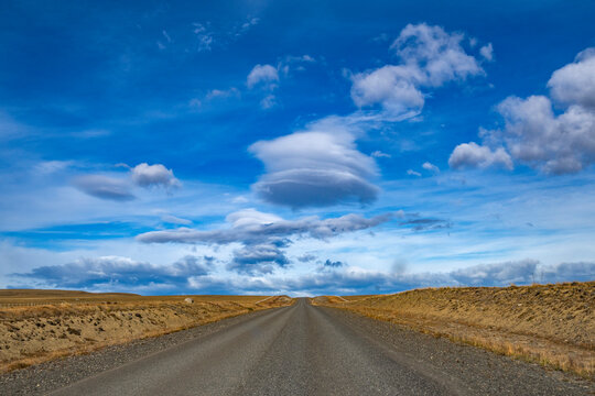 Clouds over empty road in grassy landscape