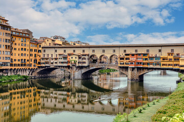 Obraz premium The Ponte Vecchio bridge in Florence showcases its colorful buildings and shops reflecting in the tranquil waters Arno river.