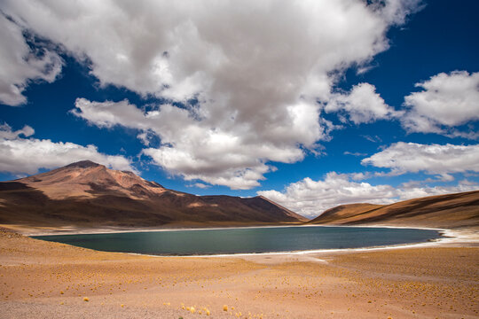 Puffy clouds over lake and barren mountains in Atacama Desert