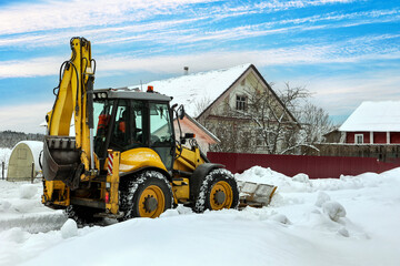 Articulated backhoe loader uses hydraulics to drive dozer blade for snow removal, while high-traction tires ensure maneuverability across snow covered terrain near buildings. © grigvovan