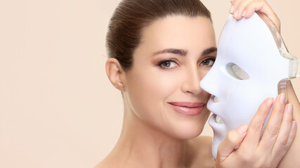 Woman smiling while holding LED facial mask for beauty and skincare treatment with photon therapy for skin rejuvenation