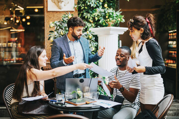 A multicultural group of business professionals discussing projects and exchanging ideas in a lively and modern coffee shop environment, reflecting teamwork, creativity, and strategy in a relaxed