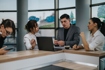 A team of business professionals engaged in a discussion around a table in a modern office. The group is focused on a laptop while interacting, suggesting teamwork, communication, and collaboration.