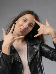Young woman in a model test, close-up shot. Natural expression, soft smile, and lively emotions. Long hair, leather jacket, neutral background. Visible skin texture, soft studio lighting