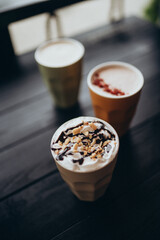 Assorted hot drinks in colorful ceramic cups with toppings on dark wooden cafe table, cozy autumn or winter beverage selection