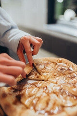 Woman picking up a slice of apple cinnamon dessert pizza from the whole pie, warm sweet pizza topped with glazed apples and caramel syrup, perfect for autumn gatherings