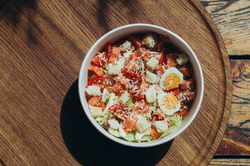 Caesar-style salad with cherry tomatoes, egg halves, croutons and grated cheese in eco-friendly bowl on wooden surface