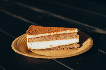 Classic slice of tiramisu cake sprinkled with cocoa powder, served on textured eco paper plate and wooden tray, warm ambient light in rustic cafe setting