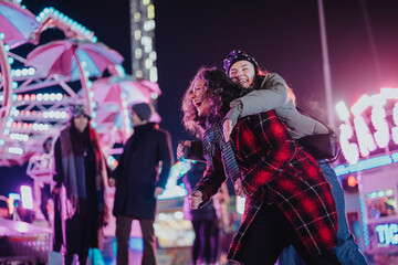Young friends having fun at a colorful night fairground, enjoying dynamic rides and a festive...