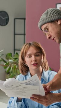 Vertical shot of film director showing script to actress and giving her tips for better acting in studio