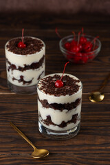 Brownie cake trifle, Black forest or Schwarzwald dessert with chocolate biscuit , whipped cream and cherries on a brown table. Vegan dessert. Vertical orientation.