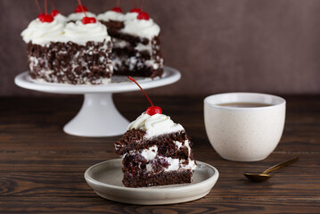 Piece of brownie cake, Black forest or Schwarzwald dessert with chocolate biscuit , cream and cherries with cup of tea on a wooden table. Vegan dessert.
