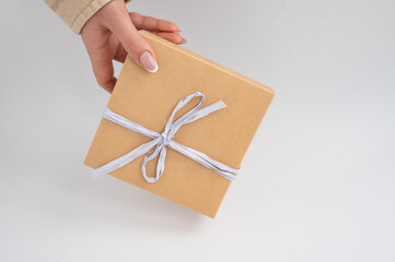 Female hand holding brown gift box with white ribbon. International Box Day