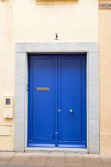 Vibrant blue door with silver frame on beige wall and sidewalk