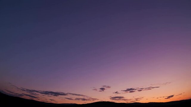 Wide-angle video capturing a serene sunset over rolling hills, showcasing a gradient sky from orange to deep blue, evoking tranquility and calm.