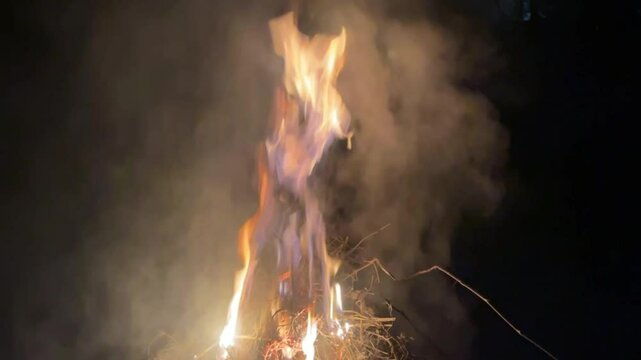 Bright firecamp with sparks at night. Fire pit outdoors, wood and dry grass on fire, flying sparks and smoke.