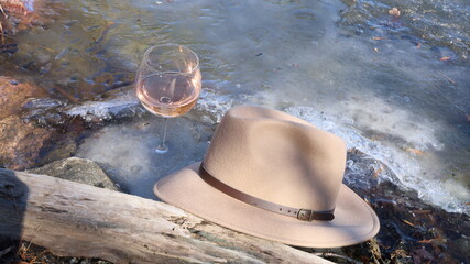glass of rose and a stylish hat sitting on a frozen lake beside a piece of driftwood