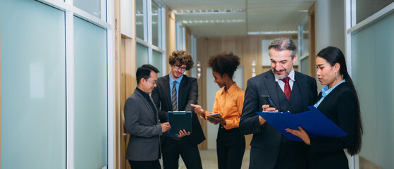 A group of different business people are sitting around a big meeting table in a modern office.