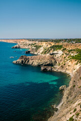 A beautiful view of the ocean with a rocky shoreline. The water is calm and clear, and the sky is a bright blue. The scene is peaceful and serene, with the ocean