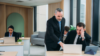 A group of different business people are sitting around a big meeting table in a modern office.