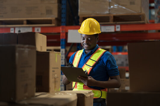 Warehouse worker, African American male warehouse worker. Male worker holding clipboard checking barcodes on product packaging boxes on shelf pallet at storage warehouse