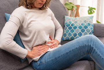 Woman experiencing abdominal pain while resting on a sofa, digestive issues or menstrual cramps