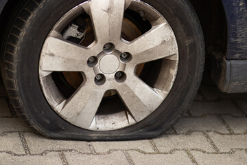 A deflated or punctured car tire with visible deformation rests on the ground. The black rubber...
