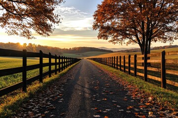 Naklejka premium A serene country road lined with wooden fences, surrounded by vibrant autumn foliage and rolling hills under a golden sunset.