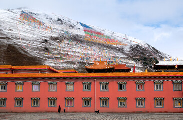 Red and imposing Tibetan Buddhist temple against the backdrop of lightly snow-capped mountains and typical colorful Tibetan flags in Tagong, Sichuan