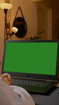 Vertical Screen: Professional businesswoman working on laptop with green screen during video conference, sitting in cozy home office environment during evening hours