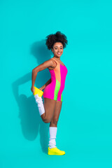 Stylish young woman wearing colorful activewear stretching against vibrant teal vertical background