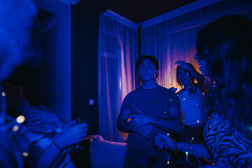 Fototapeta premium A joyful group of friends is dancing and celebrating together in a dimly lit room adorned with decorative lights, capturing a fun and dynamic atmosphere of togetherness and festivity.